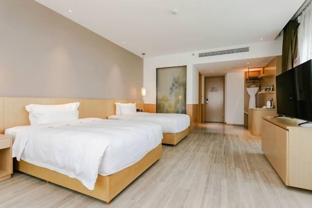 A hotel room with two beds, a desk, a TV, and a bathroom visible through an open door.