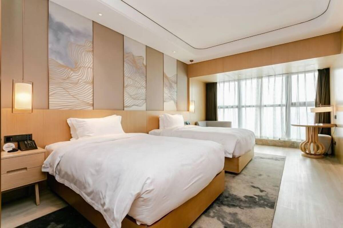 A hotel room with two beds, a nightstand, a desk, and a large window.