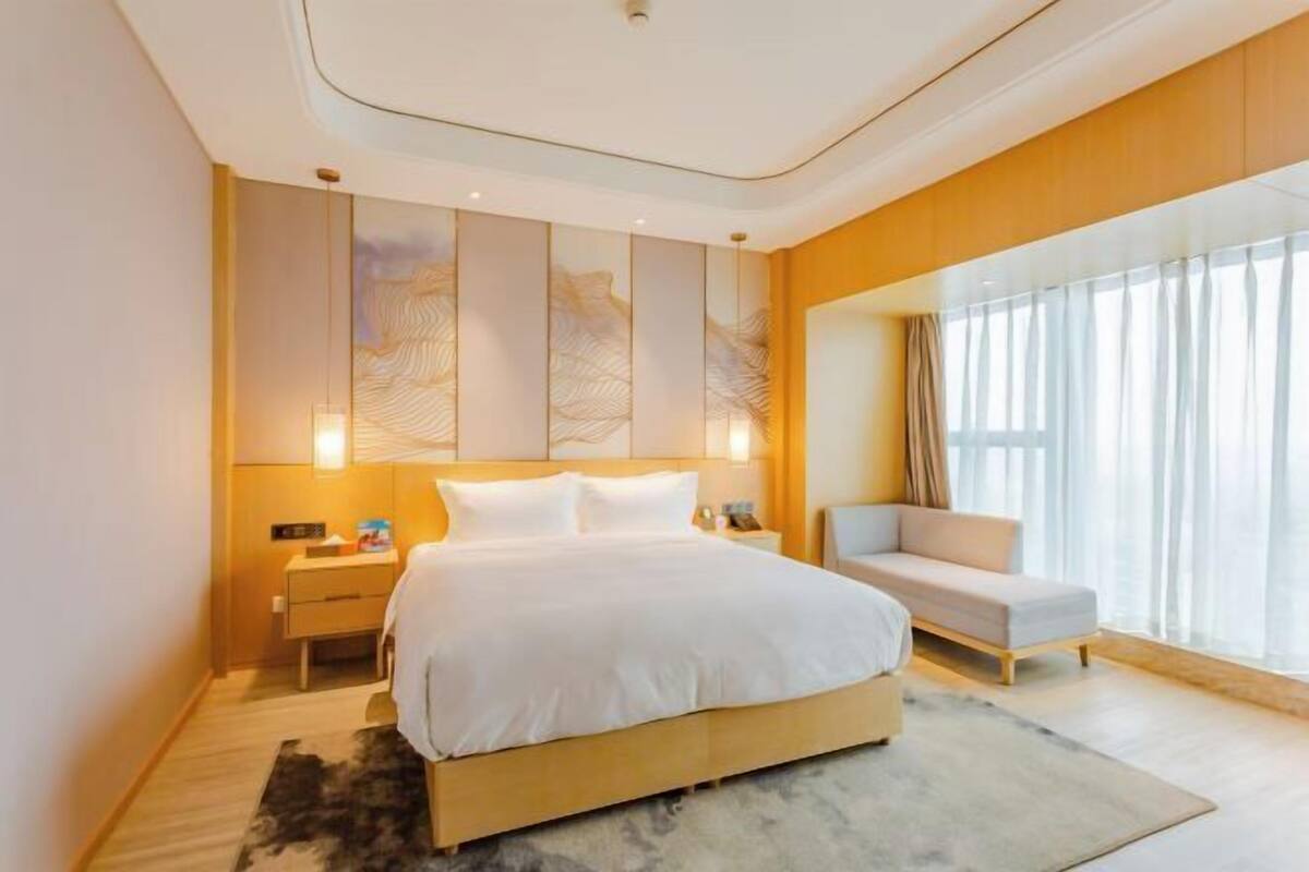 A modern bedroom with a large bed, bedside tables, a sofa, and a large window with curtains.