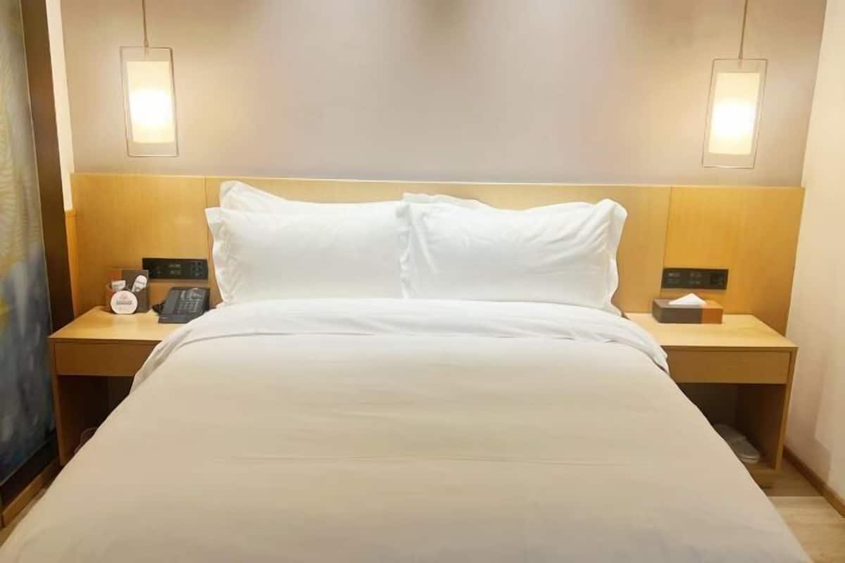 A hotel room with a large bed, two bedside tables, a nightstand, a wall-mounted telephone, and two wall-mounted lamps.