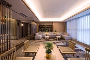 A modern living room with a sofa set, a coffee table, a dining table with chairs, a bookshelf, and a large window with curtains.