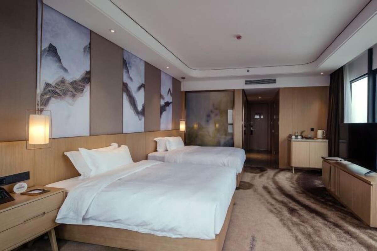 A hotel room with two beds, a desk, a TV, and artwork on the walls.