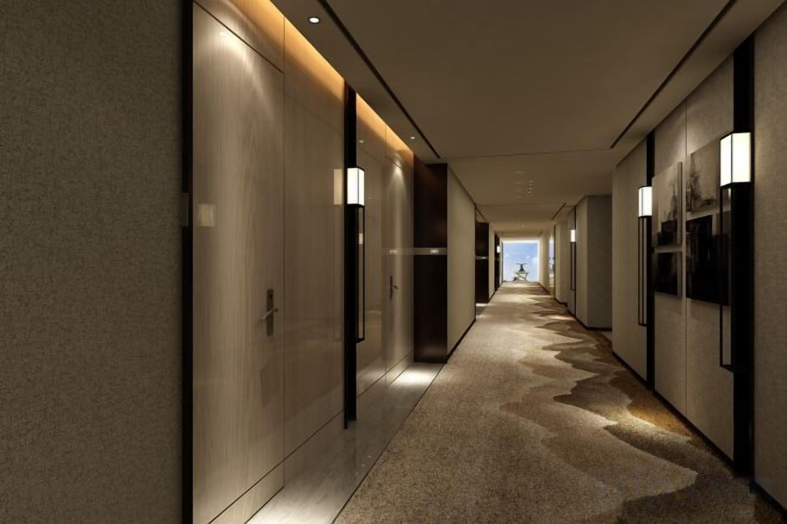 A corridor with a carpeted floor, wall-mounted light fixtures, and doors on either side.