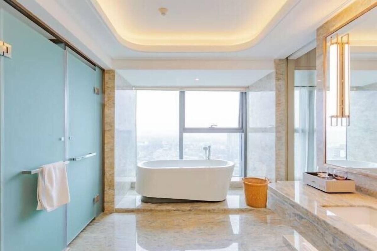 A modern bathroom with a freestanding bathtub, a large mirror, and a view of the city.
