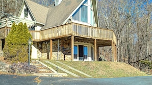 Une maison à deux étages avec une façade en pierre, une terrasse en bois et un escalier en pierre menant à l’entrée.