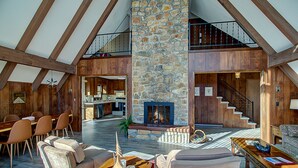 Un vaste espace de vie agrémenté d’une cheminée en pierre, de poutres apparentes et d’un coin repas avec des chaises et une table.