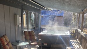 Un espace extérieur abrité comprenant un jacuzzi, des sièges et une vue sur un bâtiment dont le toit est bleu, visible au loin.
