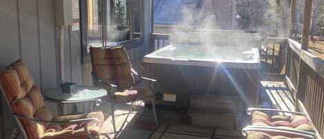 A covered outdoor area with a hot tub, seating, and a view of a blue-roofed building in the background.