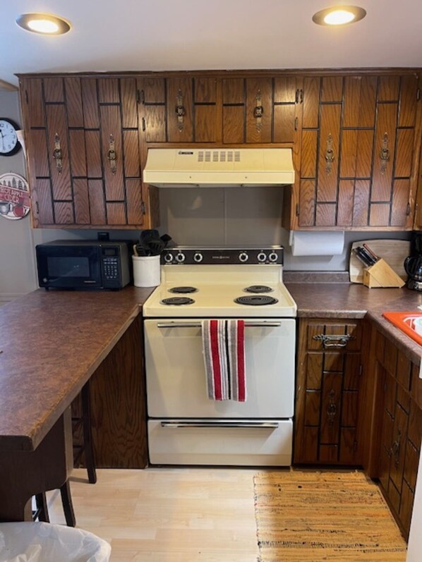 Una cocina con armarios de madera, una estufa blanca, un microondas y una encimera de madera.
