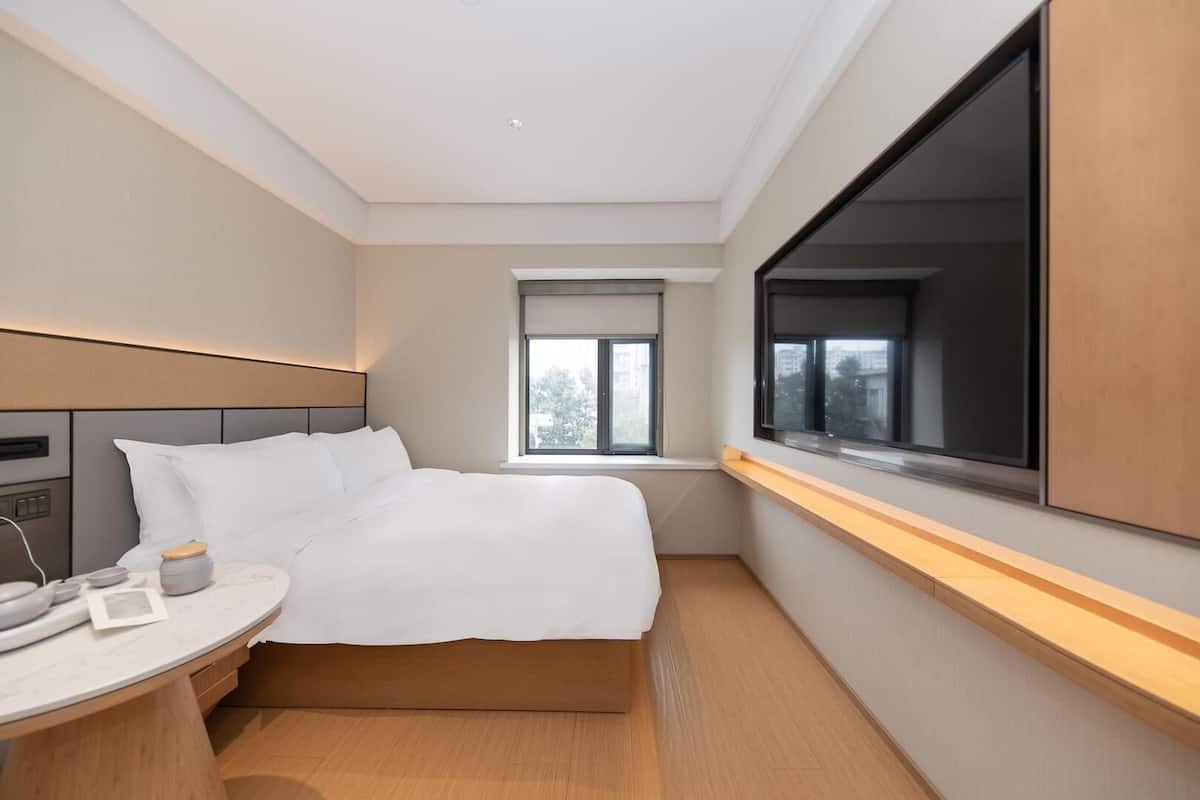 Una moderna camera d'albergo con un letto, un comodino e un'ampia finestra.