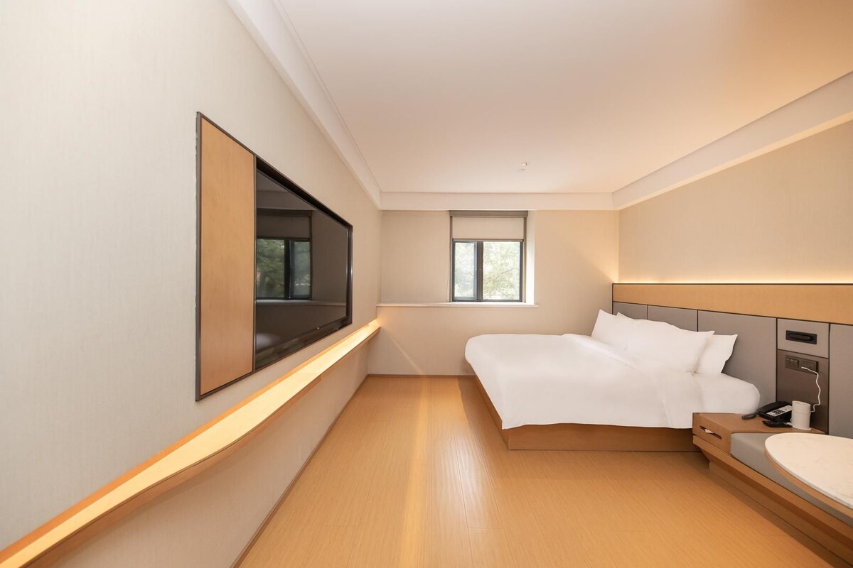 A modern hotel room with a bed, bedside table, and a large window.