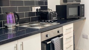 A kitchen with a black tiled backsplash, a kettle, a coffee maker, a microwave, and a toaster.