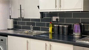 A kitchen with white cabinets, a black countertop, a stainless steel sink, a kettle, and a dish soap bottle.