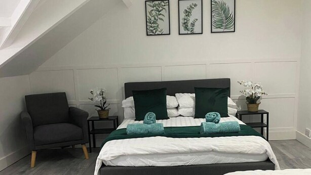 A modern bedroom with a large bed, two side tables, a chair, and framed botanical prints on the wall.
