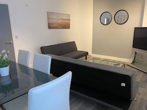 Ein modernes Wohnzimmer mit einem Glastisch, einem grauen Sofa und einem Flachbildfernseher.