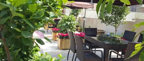 An outdoor patio with wicker furniture, potted plants, and a table under a shaded area.
