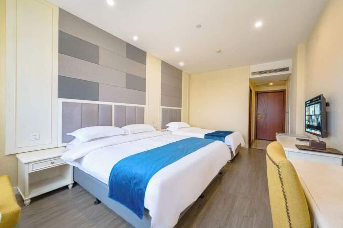Hotellihuone, jossa on kaksi sänkyä, työpöytä, televisio ja ovi, joka johtaa toiseen huoneeseen.