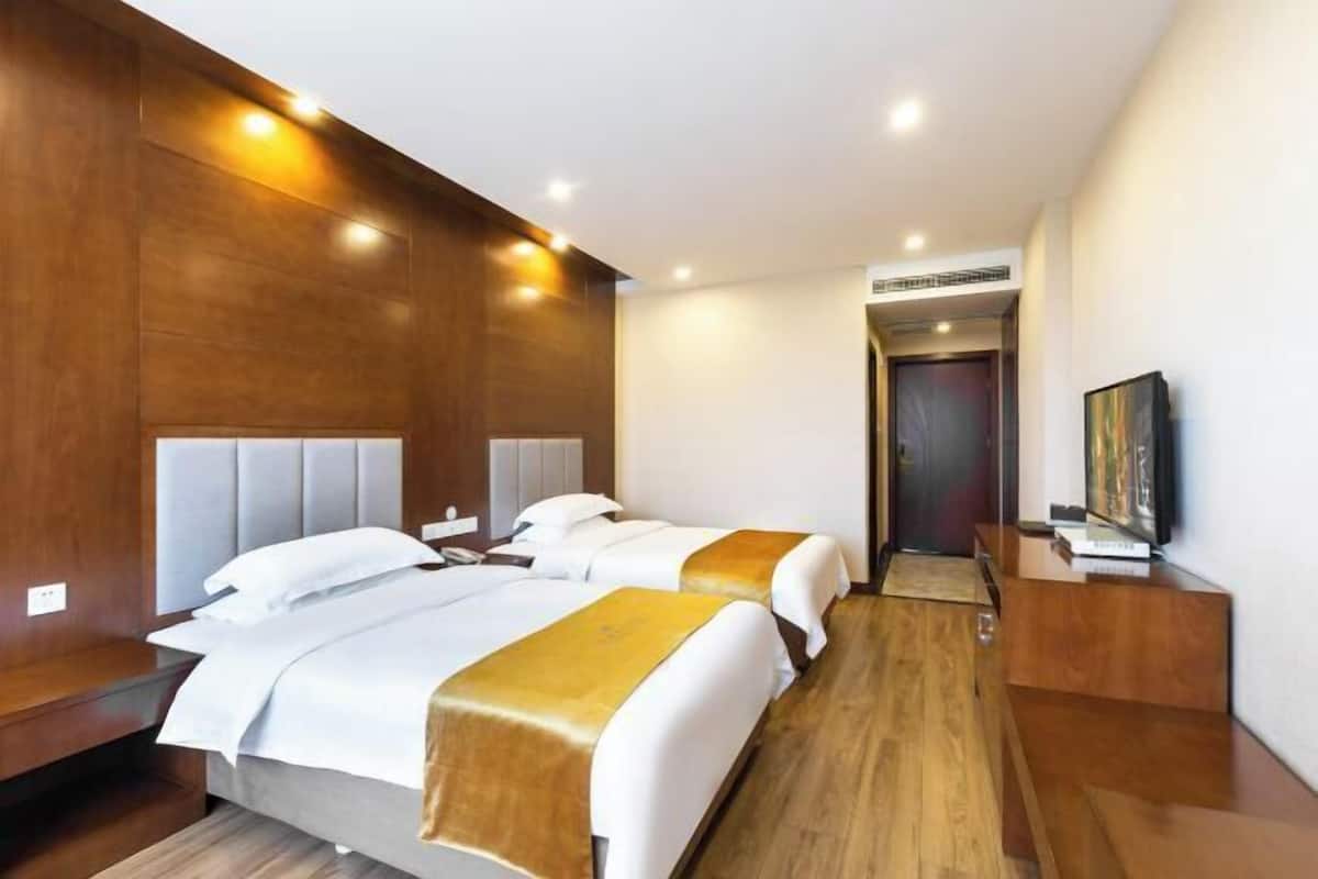 Hotellihuone, jossa on kaksi sänkyä, puupanelointi, jalustalla oleva televisio ja puinen työpöytä.