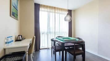 A hotel room with a dining table, chairs, a small kitchen area, and a window with curtains.