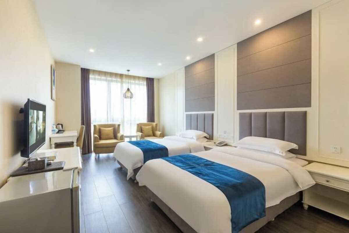 A hotel room with two beds, a desk, a TV, and a window with curtains.