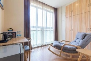 A compact room with a wooden table, a small refrigerator, a rocking chair, and a wardrobe. - Fuda Fashion Hotel (Chongqing)