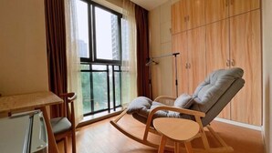 A modern living room with a large window, a wooden rocking chair, a small table, and a wardrobe. - Fuda Fashion Hotel (Chongqing)