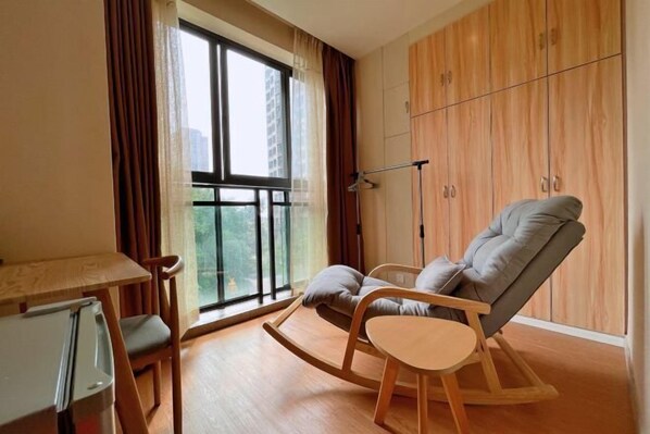 A modern living room with a large window, a wooden rocking chair, a small table, and a wardrobe. - Fuda Fashion Hotel (Chongqing)