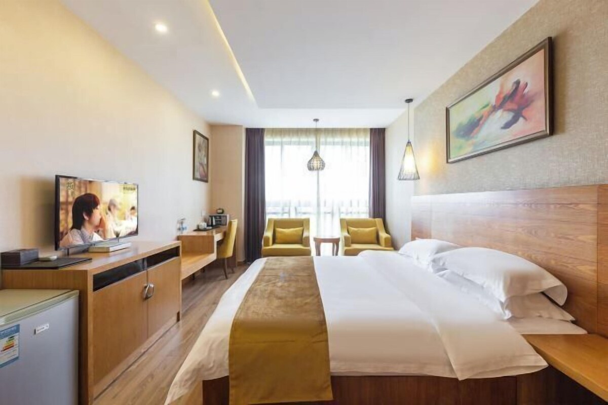 A hotel room with a bed, a desk, a chair, a television, and a window with curtains.