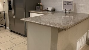 A kitchen with a stainless steel refrigerator, white cabinets, a granite countertop, and a welcome sign. - Bluedoor House Comfy Home close to NB, SA, & RAFB (Live Oak)