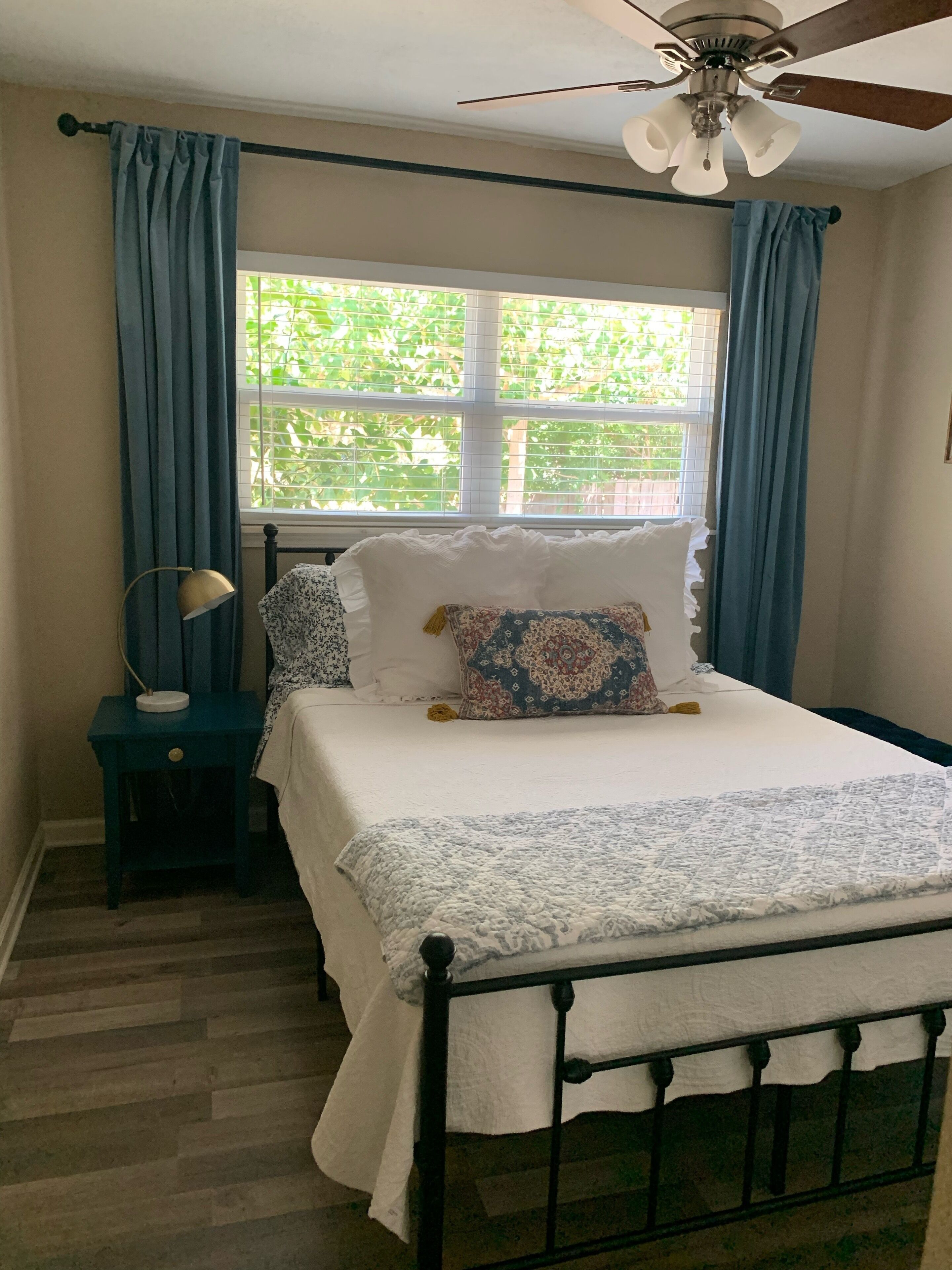A bedroom with a bed, a nightstand, a ceiling fan, and a window with curtains.