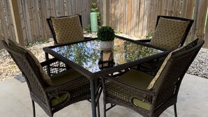 A covered outdoor patio with a glass-top table surrounded by wicker chairs with cushioned seats. - Bluedoor House Comfy Home close to NB, SA, & RAFB (Live Oak)