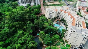 Un edificio residencial de gran altura con varios balcones, una piscina y abundante vegetación alrededor de la propiedad.
