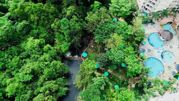 Vista aérea de un resort con múltiples piscinas, exuberante vegetación y un río.