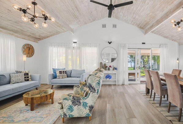 A spacious living room with a high ceiling, a dining area with a view, and a large mirror.