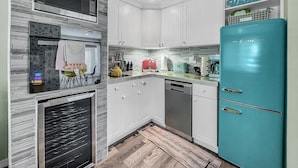 A modern kitchen with white cabinets, a teal refrigerator, and a microwave.