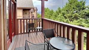 Una terraza de madera con dos sillas de mimbre y una mesa de vidrio, con vistas a un paisaje verde exuberante.