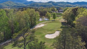 Ein Golfplatz mit Teich, umgeben von Bäumen und Bergen.