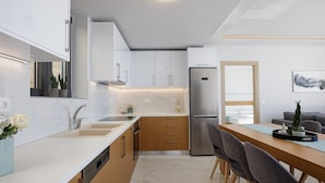 Une cuisine moderne avec des meubles blancs, un réfrigérateur en acier inoxydable et un coin repas comprenant une table et des chaises en bois.