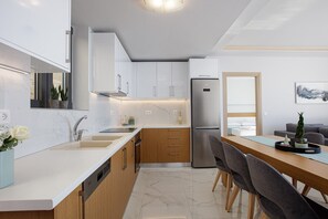 A modern kitchen with white cabinets, a stainless steel refrigerator, and a dining area with a wooden table and chairs.
