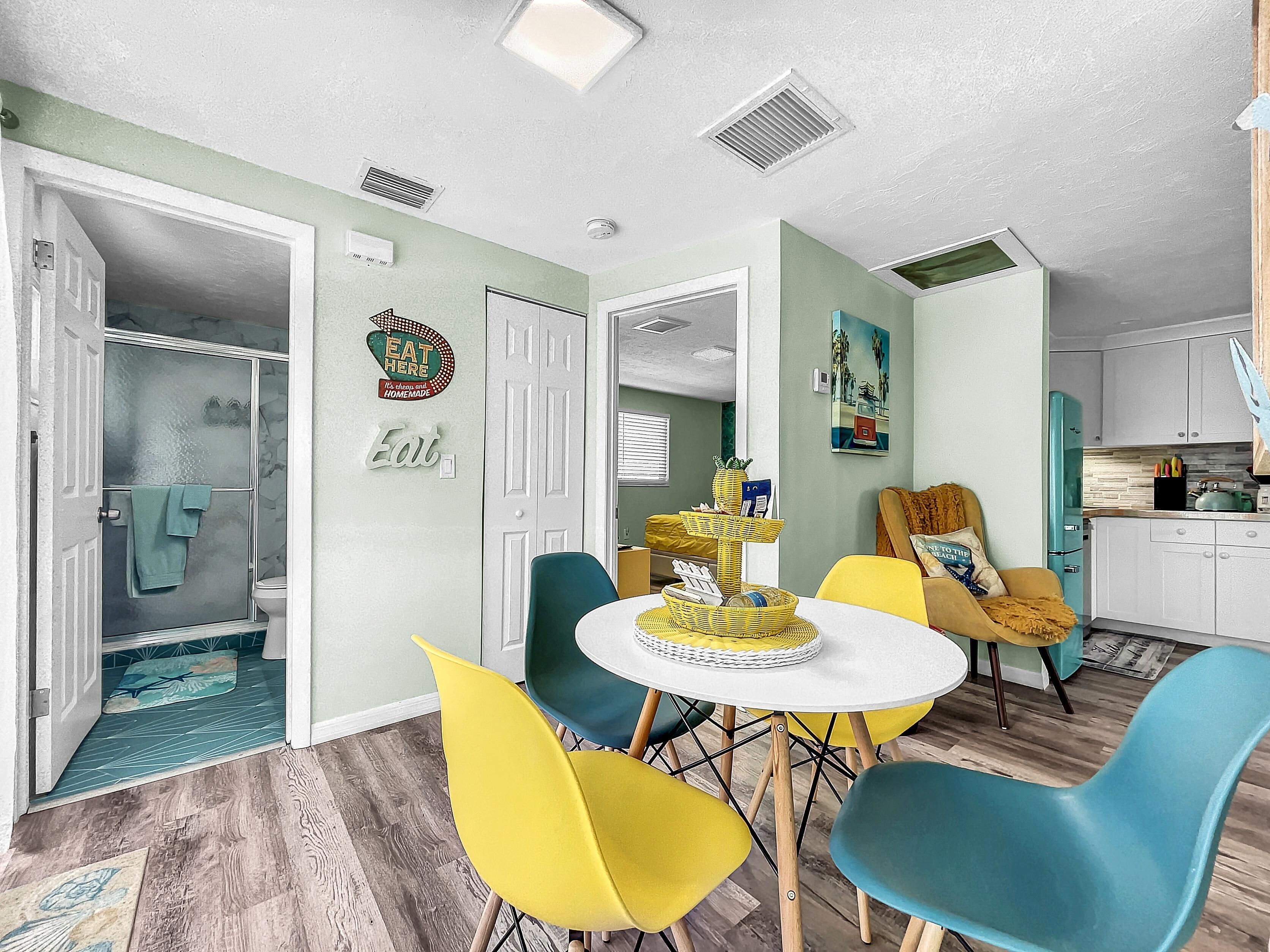 A modern kitchen with white cabinets, a teal refrigerator, and a yellow chair.