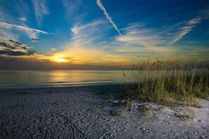 Una playa con arena y césped, una puesta de sol y un cielo despejado.