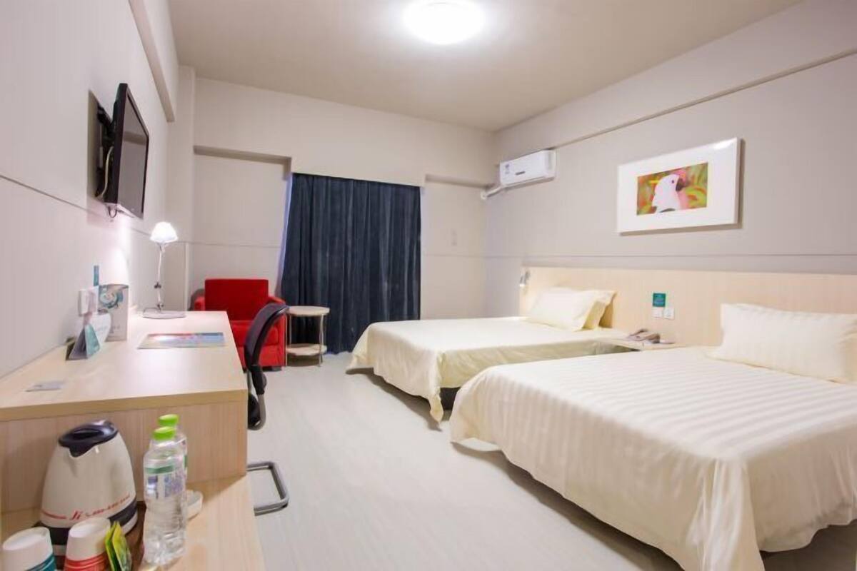 Ein Hotelzimmer mit zwei Betten, einem Schreibtisch, einem Sessel, einem Fernseher und einem Fenster mit Vorhängen.