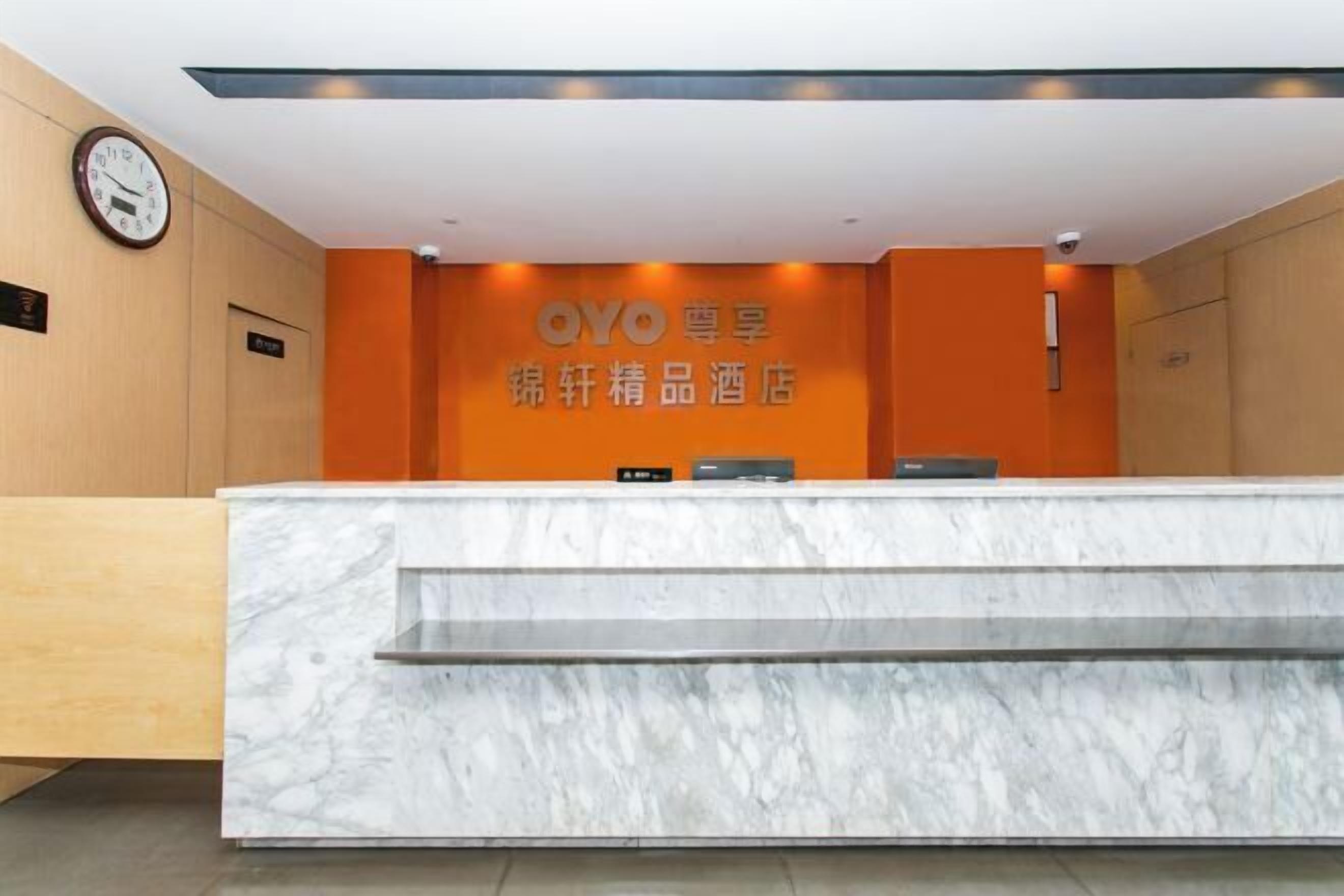 A hotel reception area with a marble counter, an orange wall with the hotel name, and a clock on the wall.