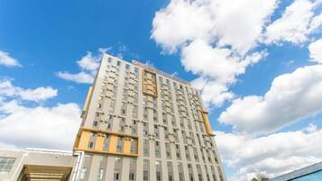 A high-rise building with multiple floors, large windows, and a clear sky with clouds.