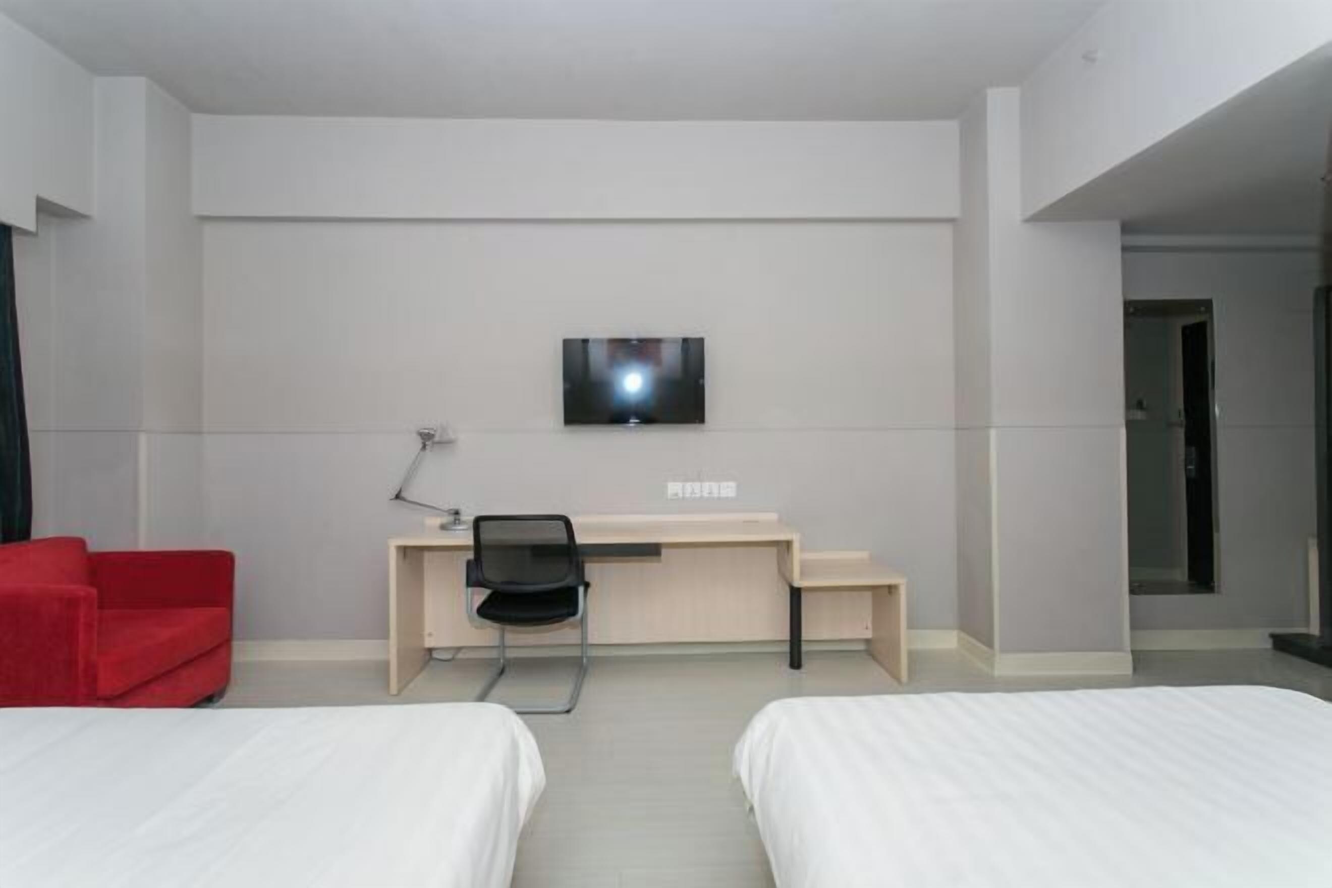 Een hotelkamer met twee bedden, een bureau met stoel, een aan de muur bevestigde televisie en een rode fauteuil.