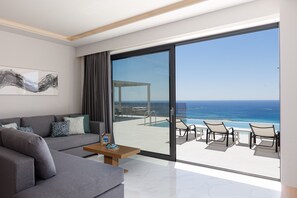 Un soggiorno moderno con un divano grigio, un tavolino da caffè e un'ampia porta vetrata che si apre su un balcone con piscina e vista sull'oceano.