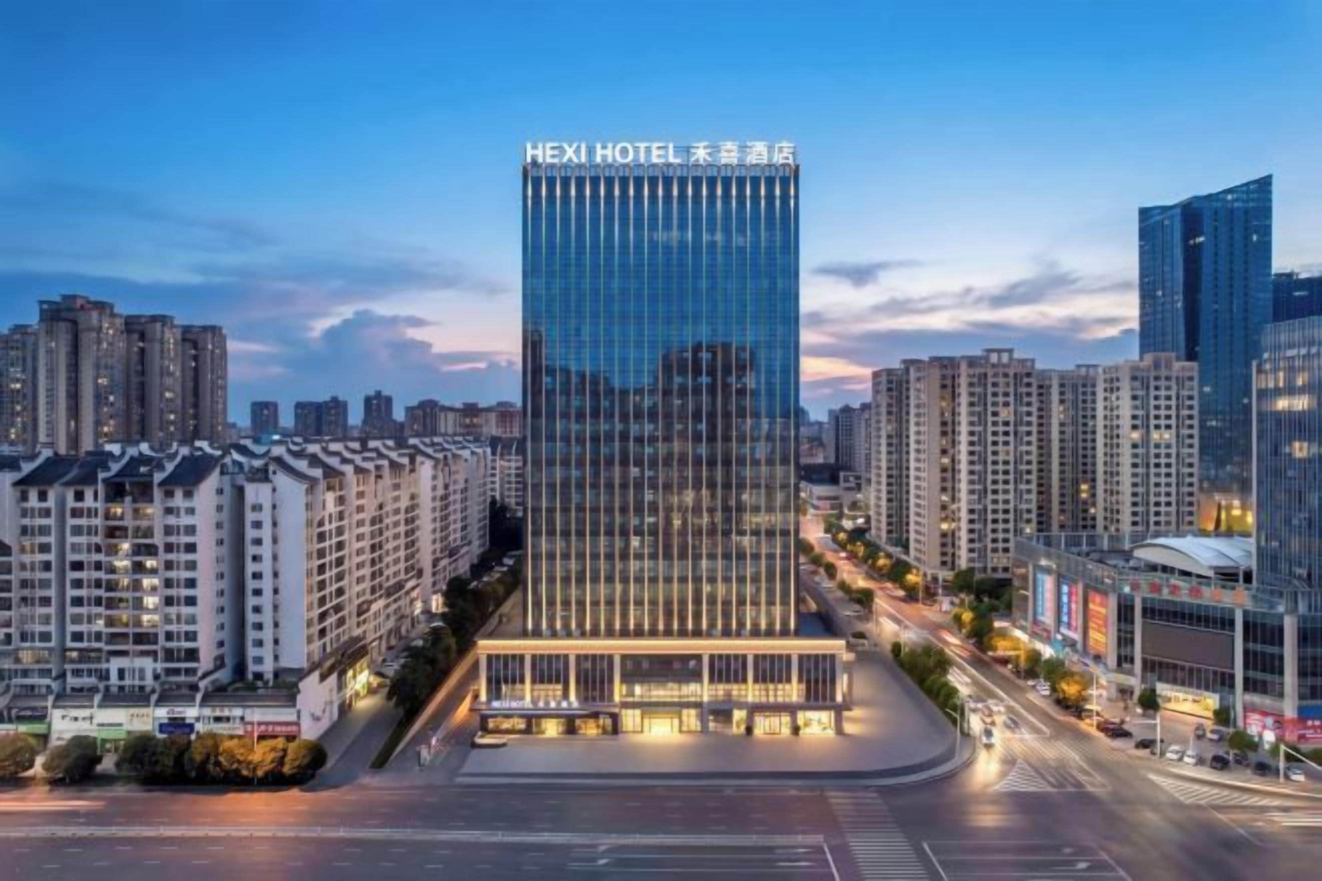 Un hotel moderno con una fachada de vidrio destacada, ubicado en un entorno urbano con edificios altos circundantes.