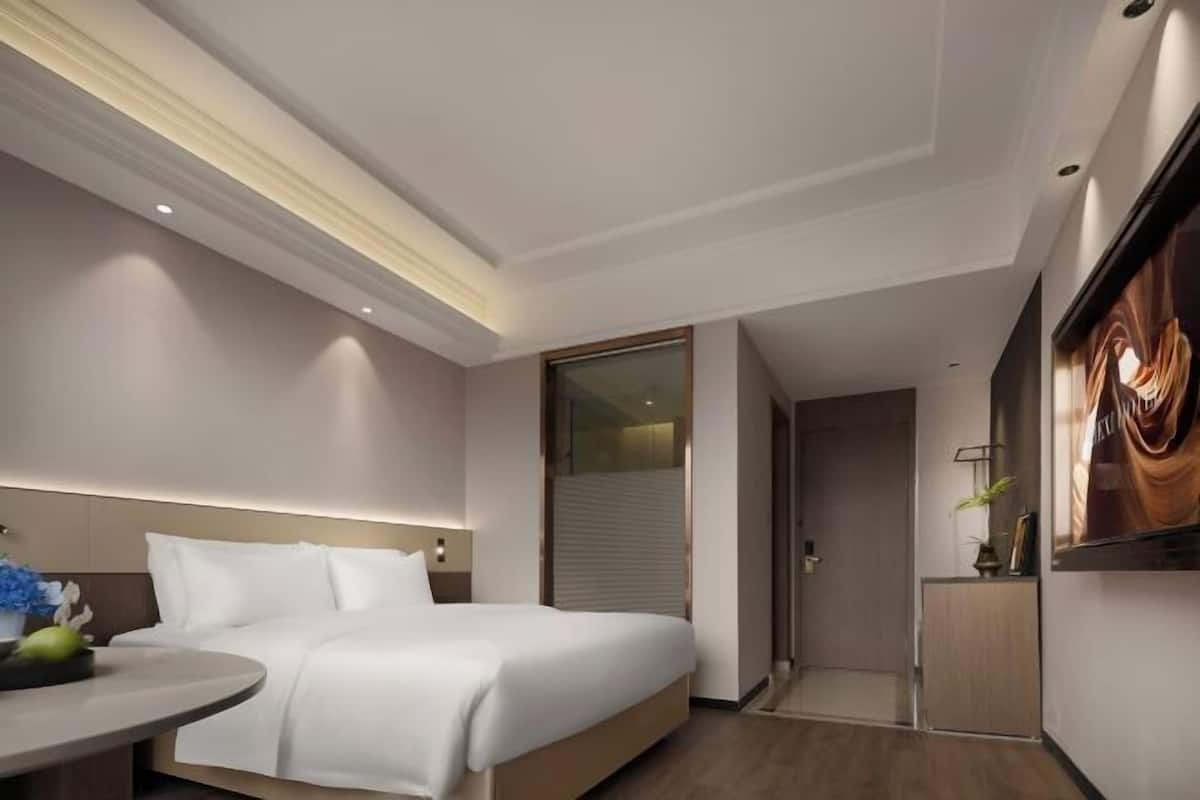 A modern hotel room with a large bed, a bedside table, a small round table, and a shower area.