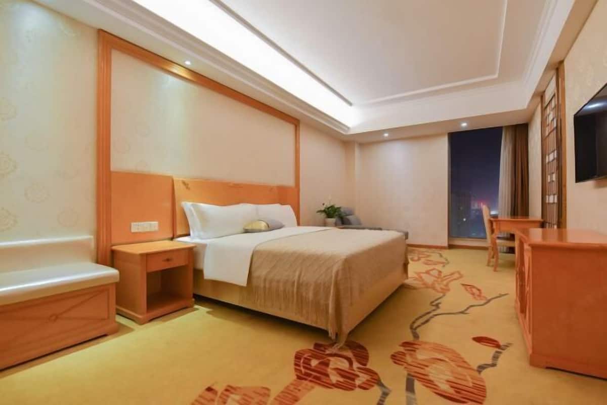 A hotel room with a bed, bedside table, and a small desk.