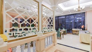 Eine Hotellobby mit modernem Design, inklusive eines geometrisch gemusterten Raumteilers, einer Chandelierleuchtre und einem Essbereich mit Tischen und Stühlen.